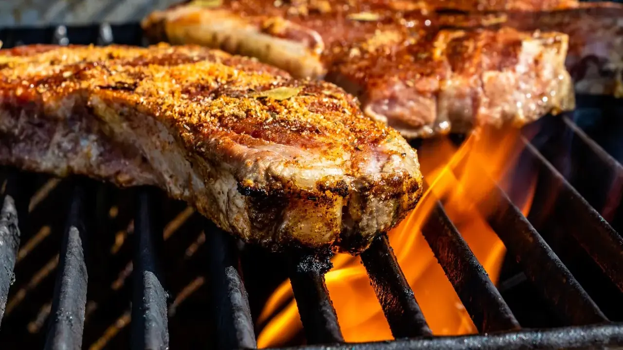 Des morceaux de viande savoureux, assaisonnés, grillent sur un barbecue, les flammes léchant les entrecôtes.