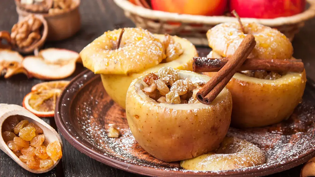 Manzanas asadas rellenas de pasas y canela, espolvoreadas con azúcar glas. Un postre casero y reconfortante.