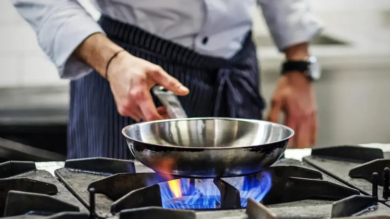 Chef calienta sartén de acero inoxidable para cocinar sobre llama azul de gas.