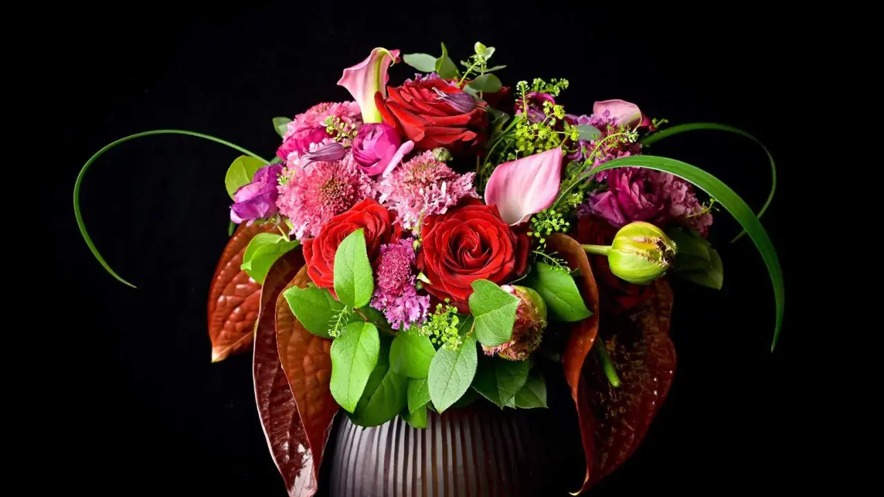 Un bouquet de roses rouges, callas roses et fleurs violettes dans un vase sombre. La signification des fleurs est souvent liée à l'amour et à la passion.