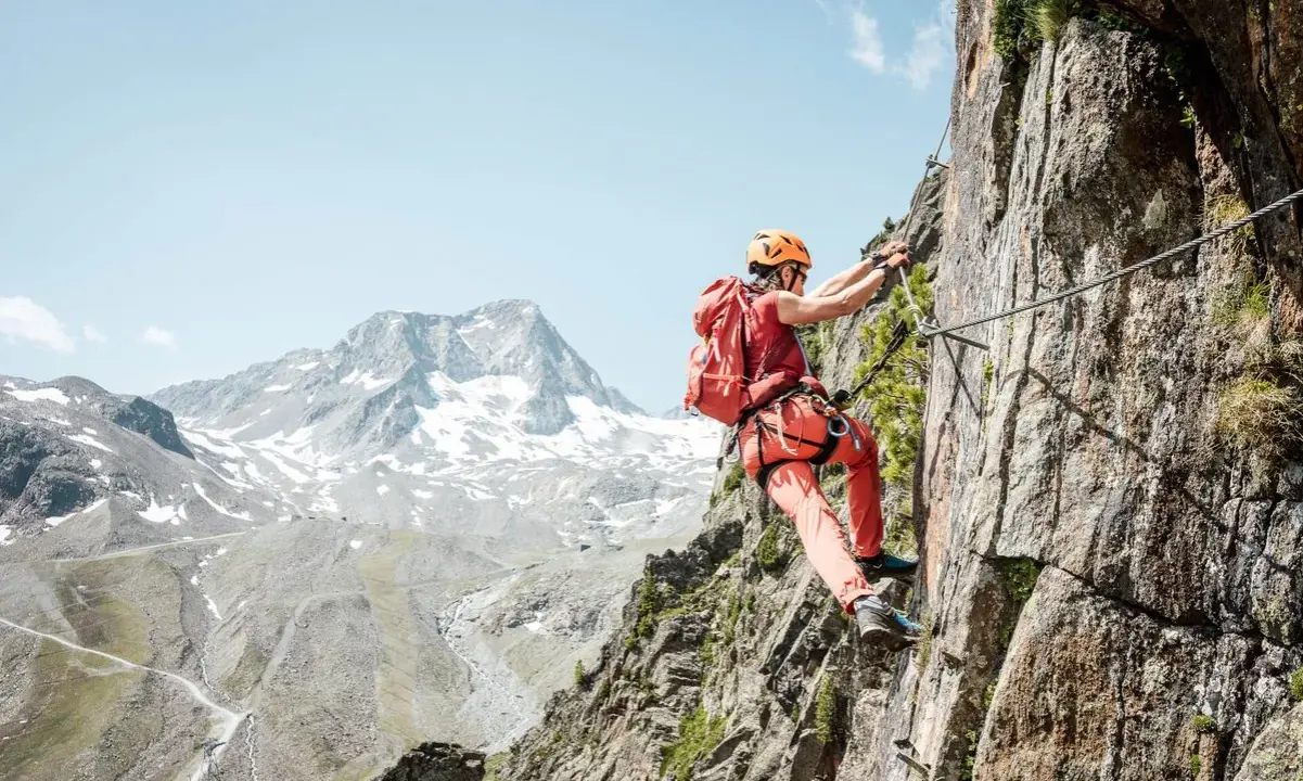 Wspinaczka po skalnej ścianie na via ferrata w Niemczech. Widok na ośnieżone góry w tle.