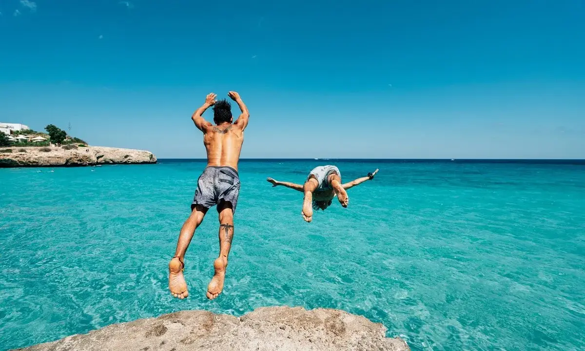 Due ragazzi si tuffano in un mare cristallino, un'idea perfetta per chi cerca dove andare in vacanza con pochi soldi in Italia.
