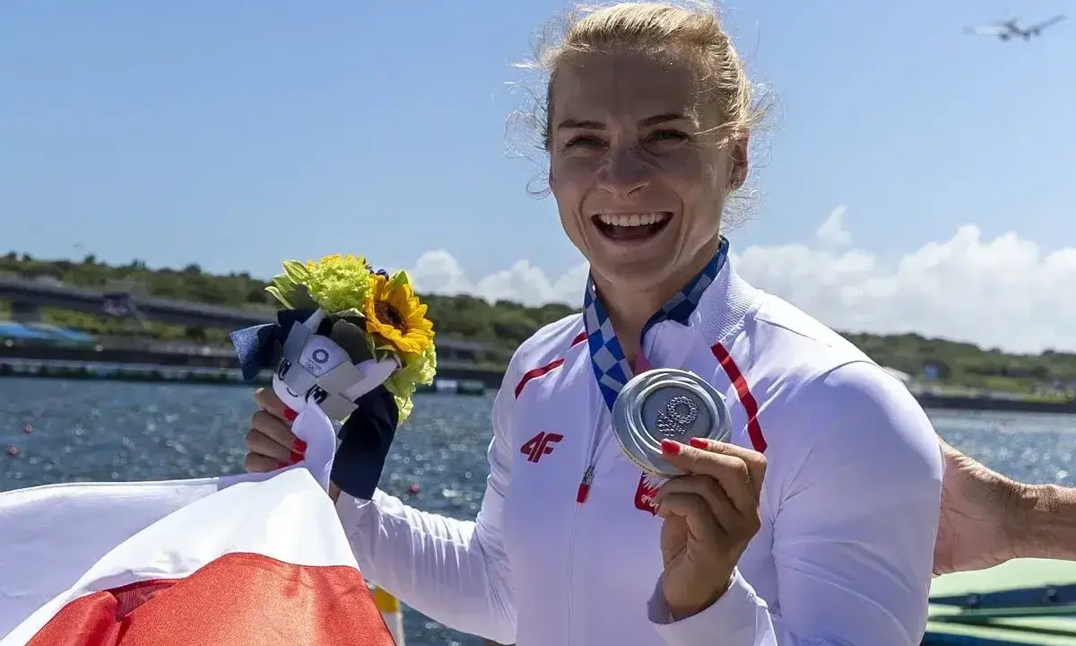Uśmiechnięta sportsmenka z medalem i bukietem kwiatów, symbol sukcesu najlepszych polskich kajakarzy.