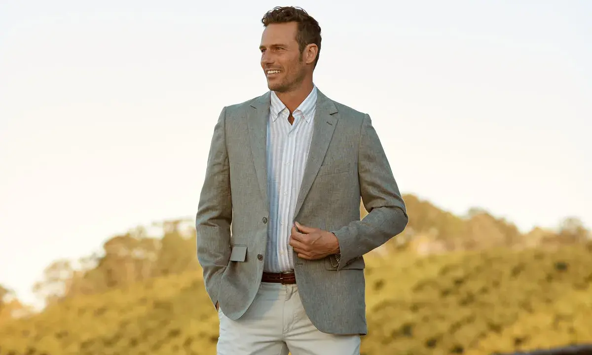 A man in a light grey blazer, striped shirt, and beige pants. This is a stylish option for what to wear to an engagement party.