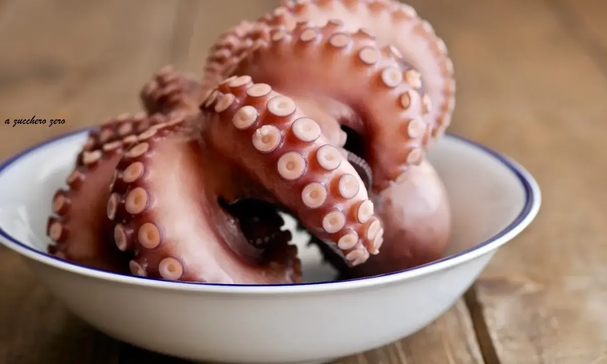 Pulpo listo para cocer en un cuenco blanco con borde azul, sobre una mesa de madera rústica.