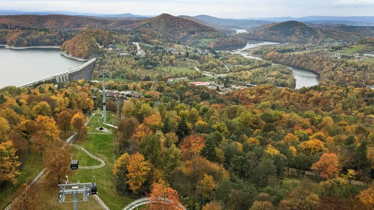 Jesienna panorama z widokiem na zaporę w Solinie i kolejkę gondolową. W oddali jezioro i góry.
