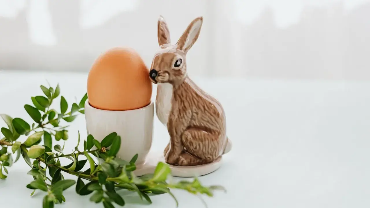 Wielkanocne jajka w kieliszku, obok ceramiczny zajączek i gałązka bukszpanu.