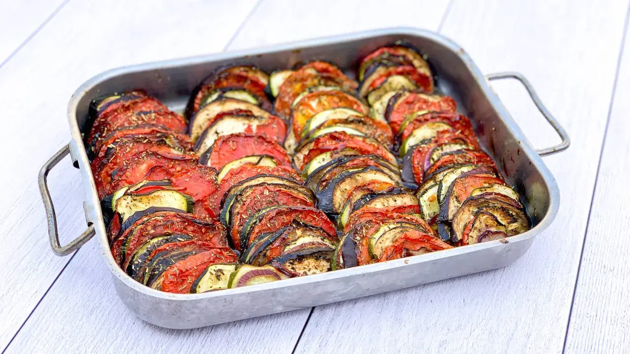 Un plat de tian de légumes, prêt à cuire, avec des rondelles de courgettes, aubergines et tomates joliment disposées. Parfait pour faire un tian de légumes la veille.