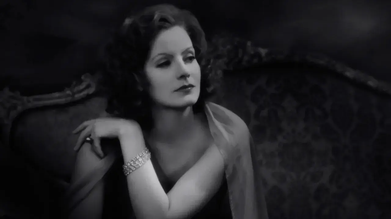 Elegancka Greta Garbo, z błyszczącą bransoletką, spogląda zamyślona z antycznej kanapy.
