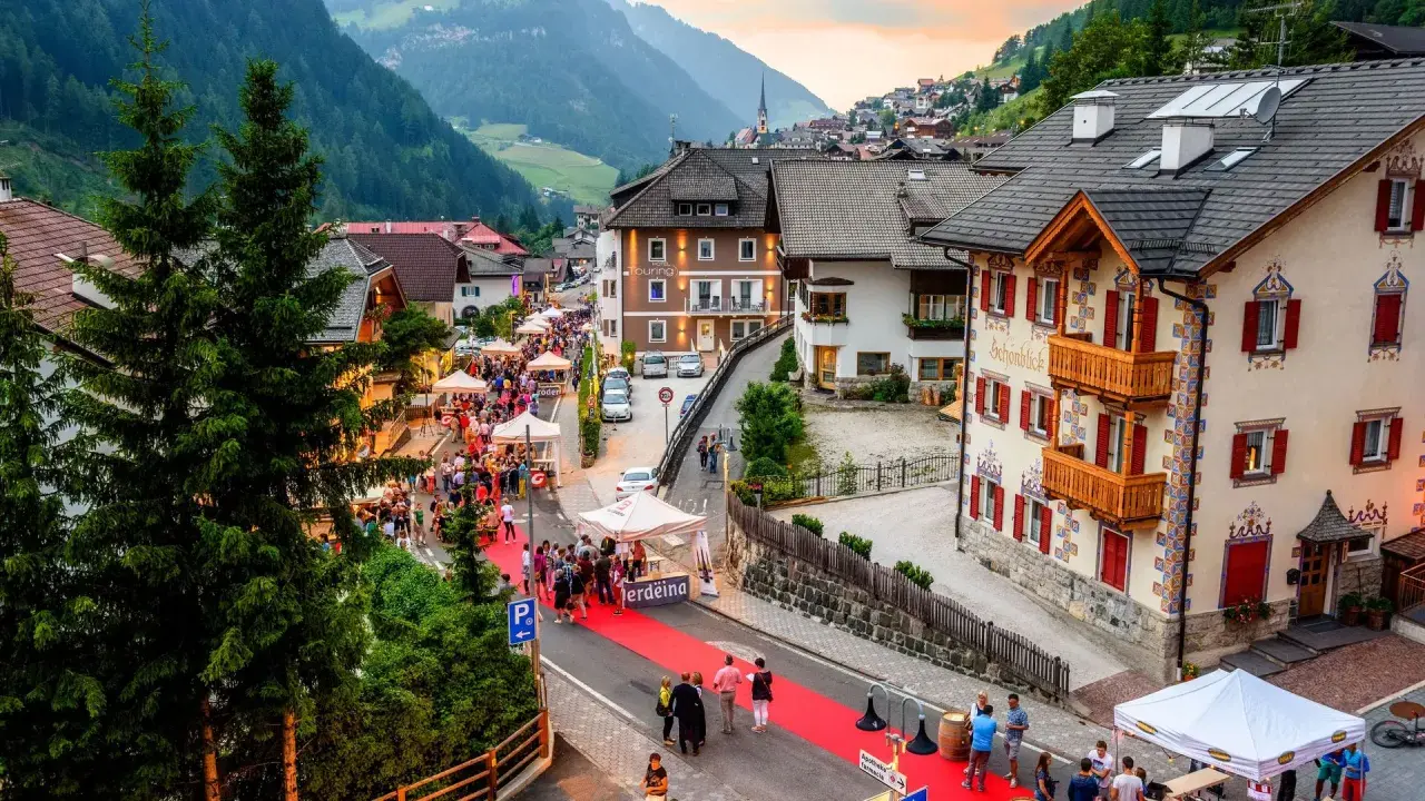 Festa a Santa Cristina Val Gardena con gente, bancarelle e un tappeto rosso.