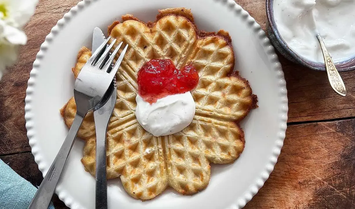 En vacker, hjärtformad våffla, perfekt för en fika. Dessa glutenfria våfflor serveras med vispad grädde och sylt.