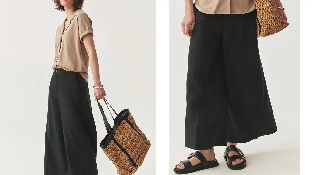 Kobieta w czarnych, szerokich spodniach i beżowej koszuli. W dłoni trzyma plecioną torbę. Wskazówka, jak odróżnić spodnie damskie od męskich.