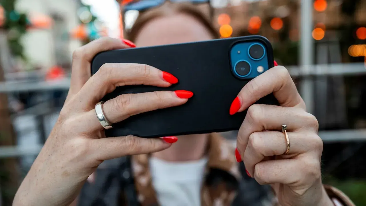 En person med röda naglar håller en iPhone. Tänk på att spionprogram iPhone kan vara ett hot mot din integritet.