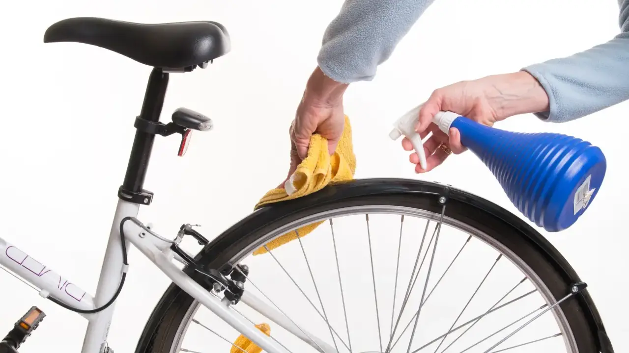 Czyszczenie piasty roweru. Ręce z żółtą ściereczką i niebieskim spryskiwaczem dbają o rower.