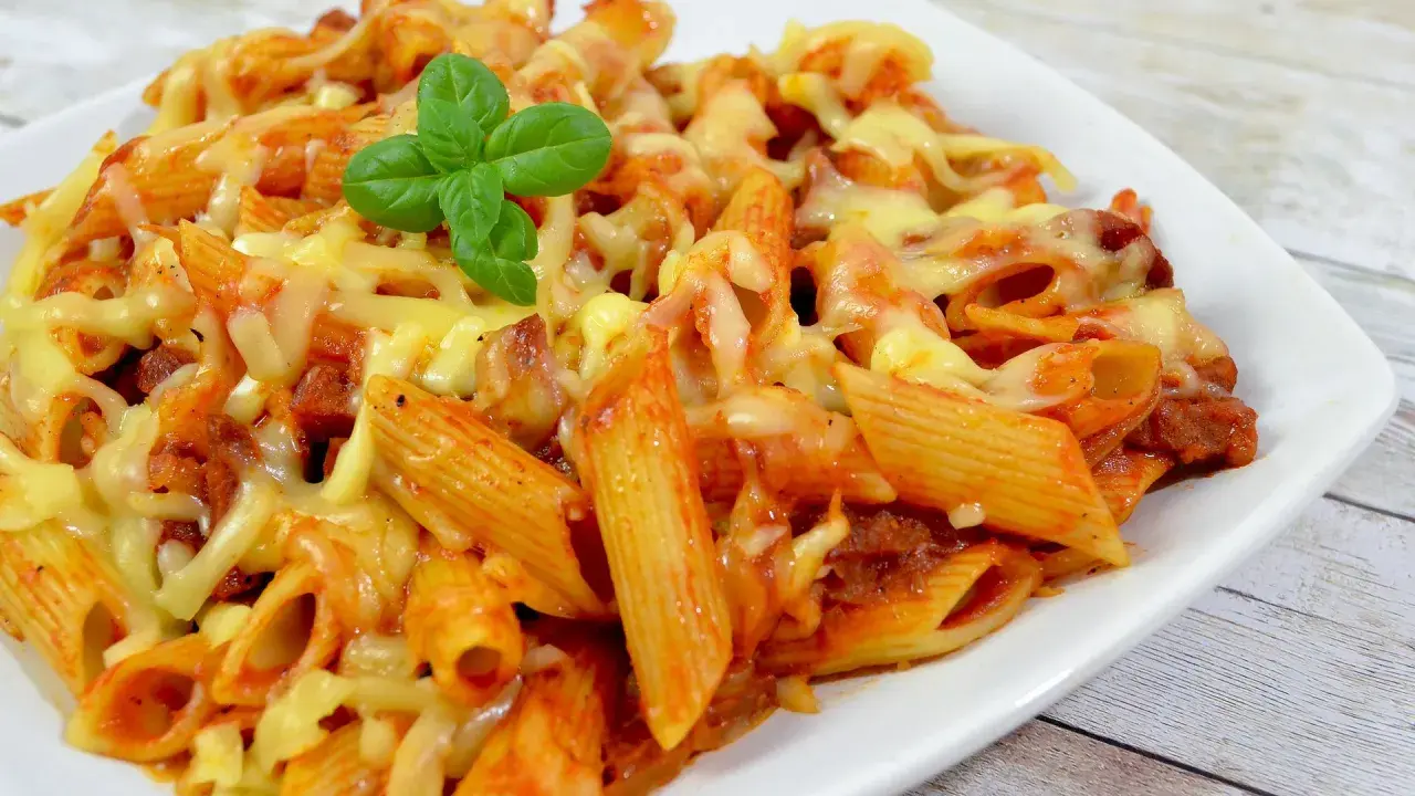 Penne z sosem pomidorowym i kawałkami pikantnego chorizo, zapieczone pod ciągnącym się serem, ozdobione listkiem bazylii.