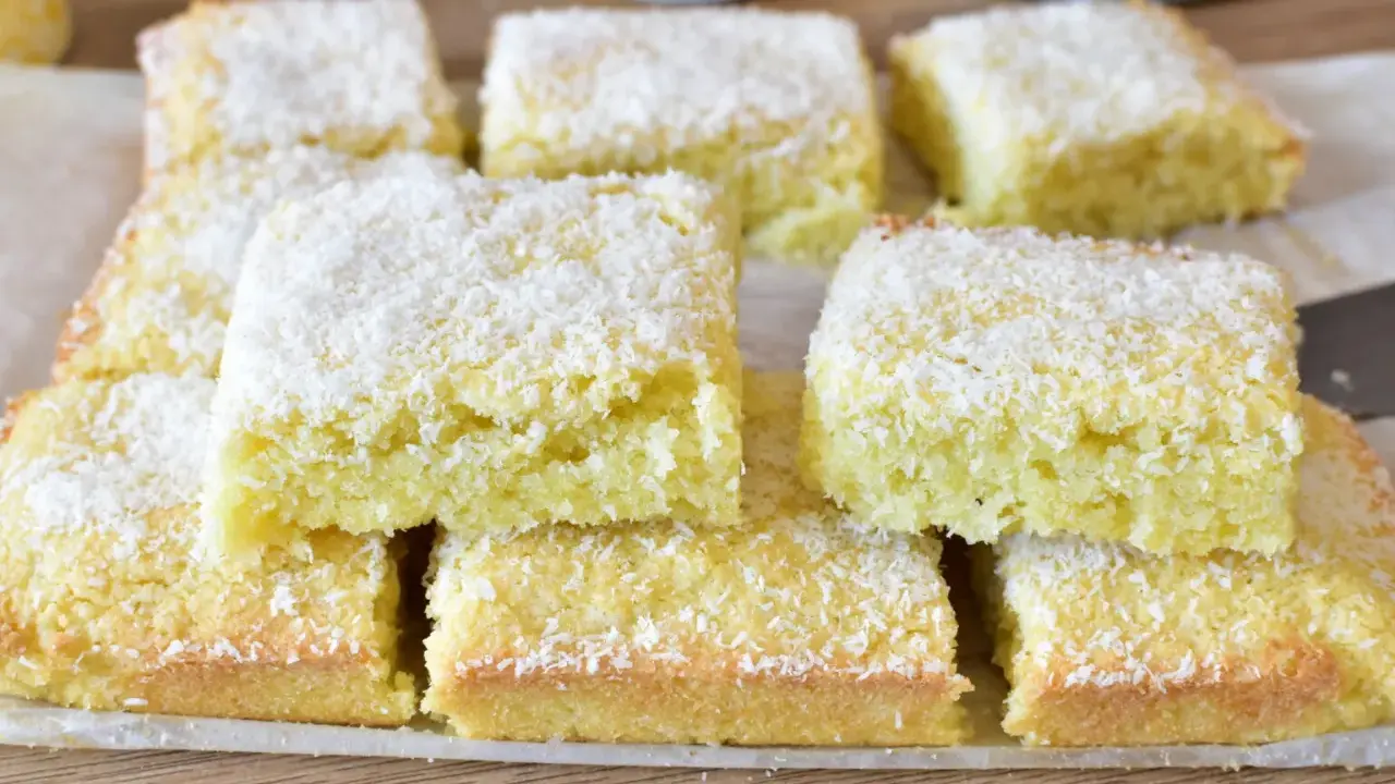 Fette di torta al cocco, soffici e dorate, cosparse di scaglie bianche. Un dolce profumato e invitante.