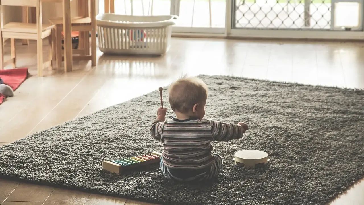 Liten bebis sitter på en matta och leker med en xylofon och en tamburin. En perfekt start på en checklista bebis för musikaliska äventyr.