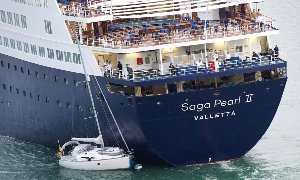 La nave da crociera "Saga Pearl II" è imponente accanto a una piccola barca a vela, mostrando la differenza tra nave e traghetto.