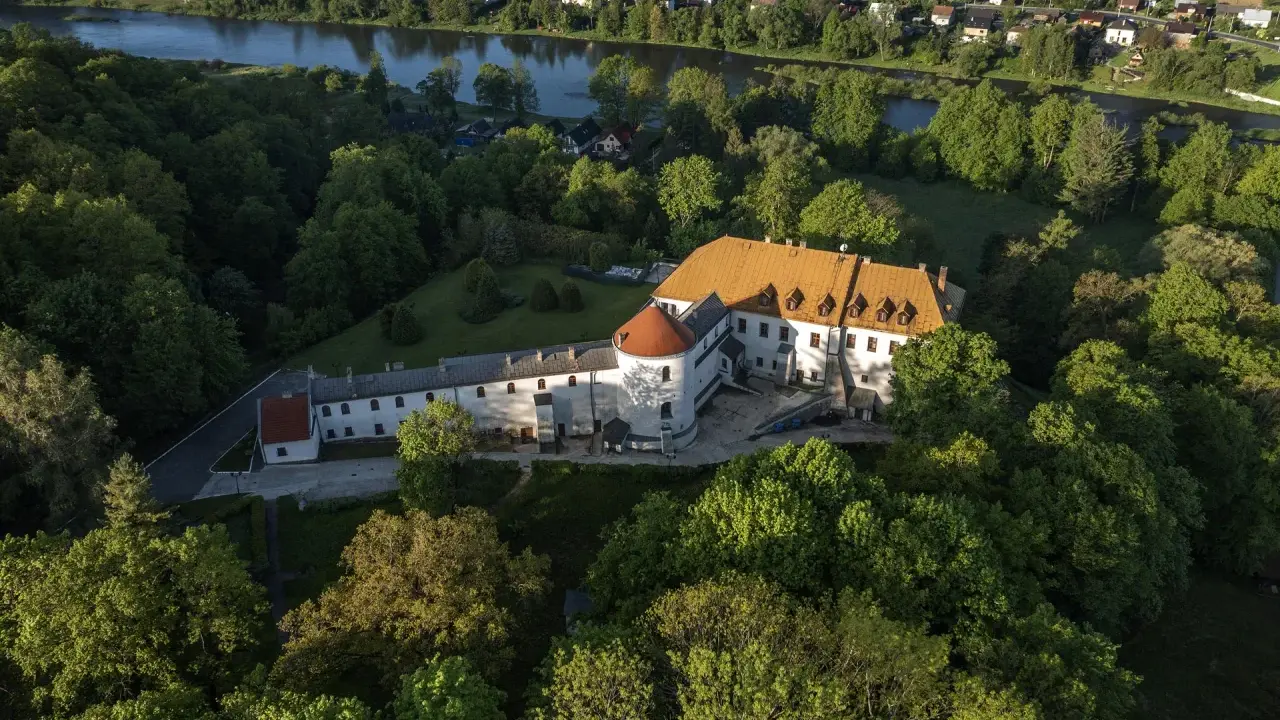 Zamek w Lesku otoczony zielenią, z widokiem na rzekę i miasteczko.