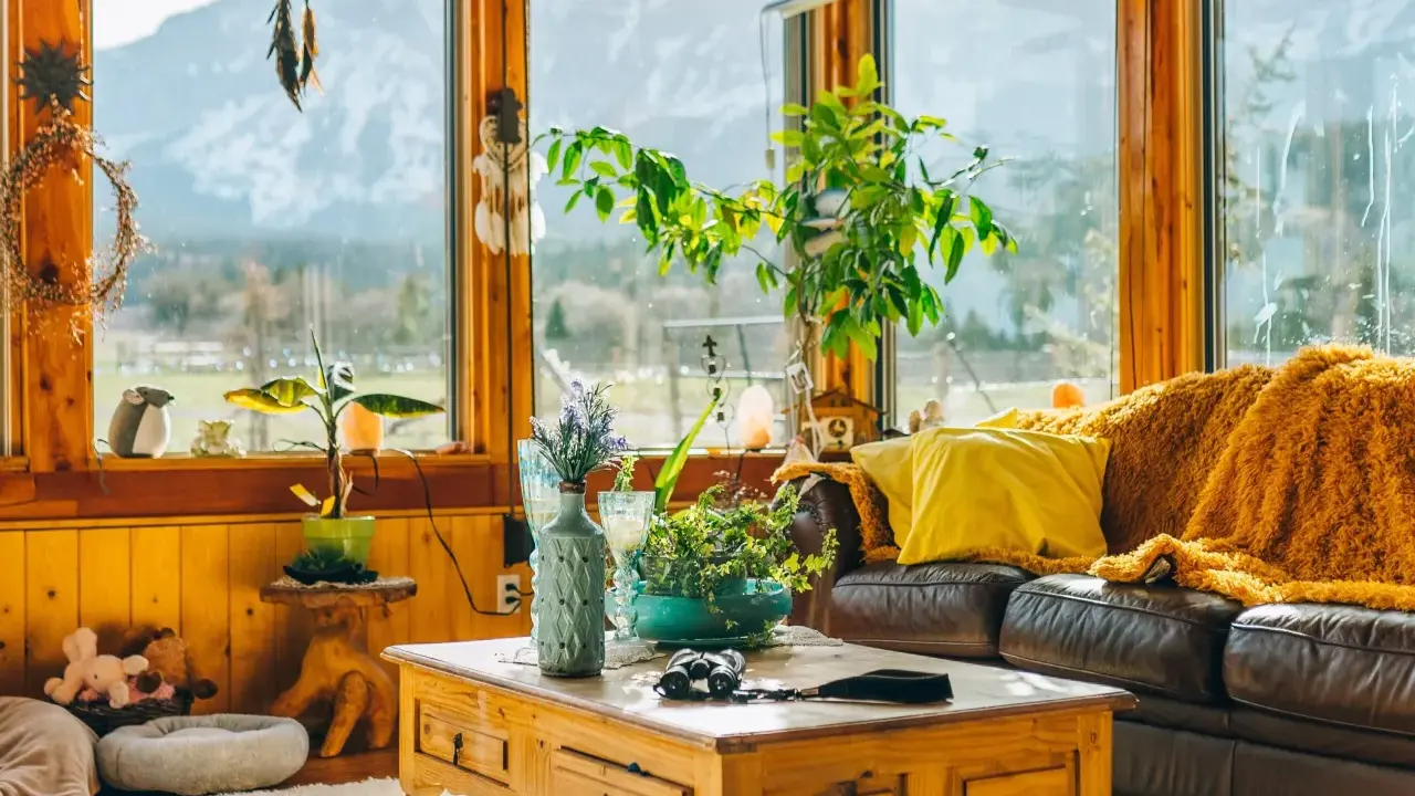 Un acogedor **salón estilo natural** con sofá de cuero, manta naranja, plantas y vistas a la montaña.