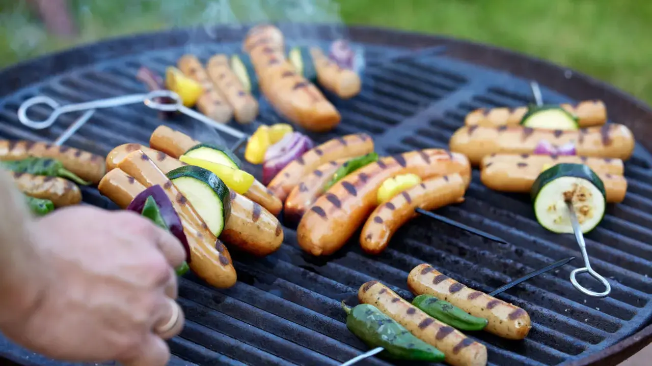 Grilla korv med grönsaker på en kolgrill. Röken stiger från den saftiga maten.