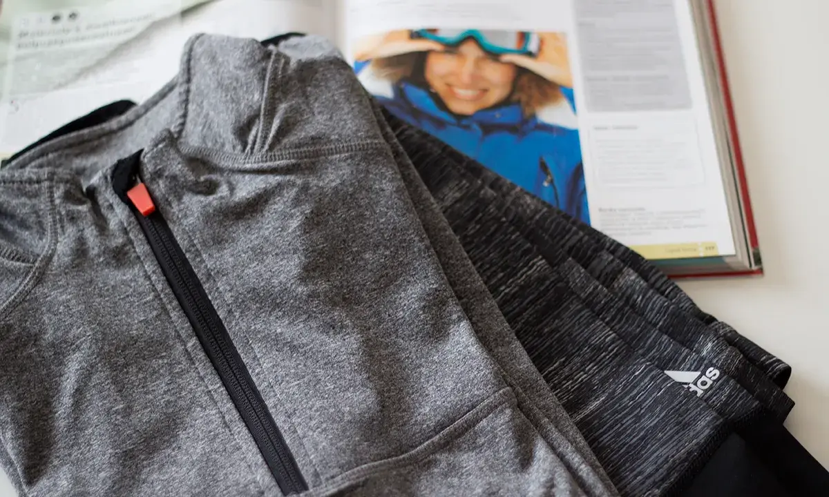 Szare spodnie sportowe Adidas obok otwartej książki z narciarką. Czy poliamid to dobry materiał na odzież sportową?