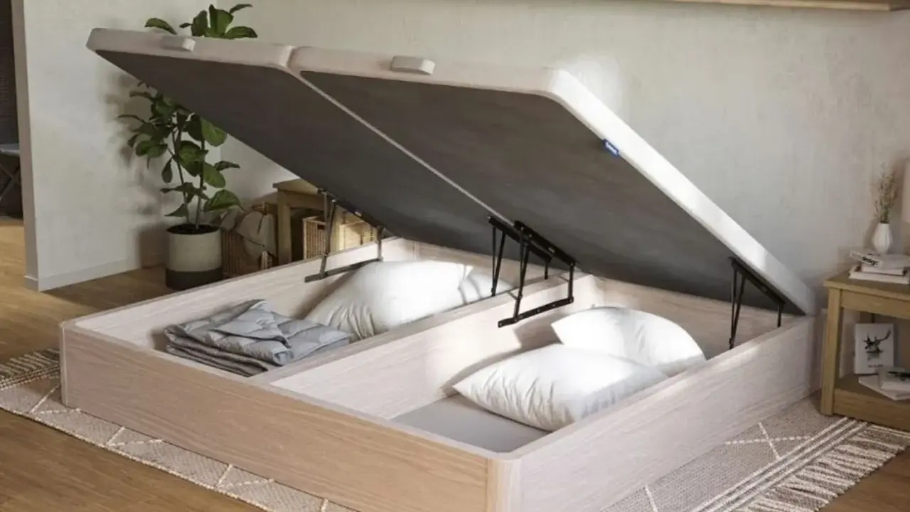 Un canapé de madera clara con la tapa abierta, revelando un gran espacio de almacenamiento para ropa de cama y almohadas.