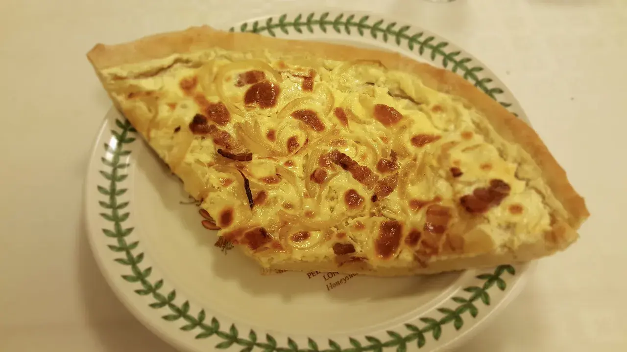 Part de quiche lorraine, une des spécialités lorraines, sur une assiette décorée de feuilles vertes.