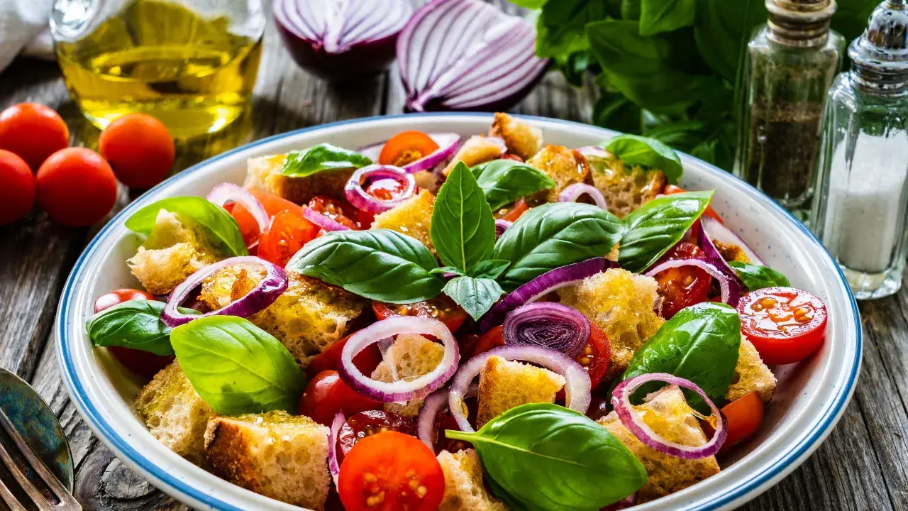 Panzanella ricetta: un'insalata estiva con pane raffermo, pomodorini, cipolla rossa e basilico fresco, condita con olio d'oliva.