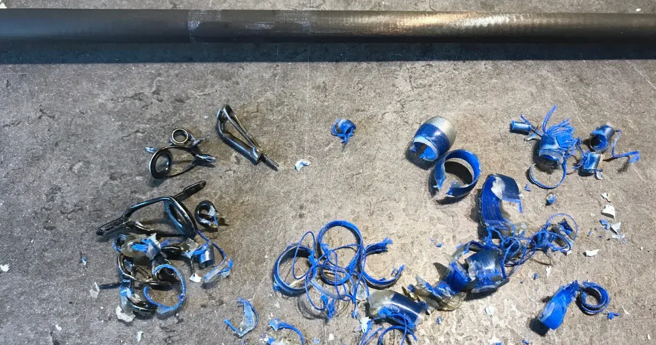 Metalowe przelotki do wędki leżą na szarym blacie, obok niebieskich wiórów i kawałków plastiku.