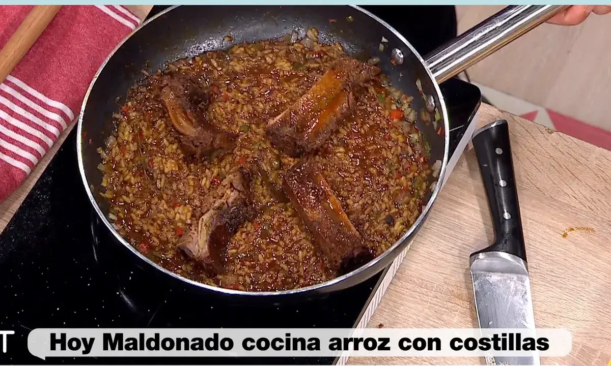 Un delicioso arroz con costillas se cocina en una sartén, con trozos de carne jugosa y arroz dorado.