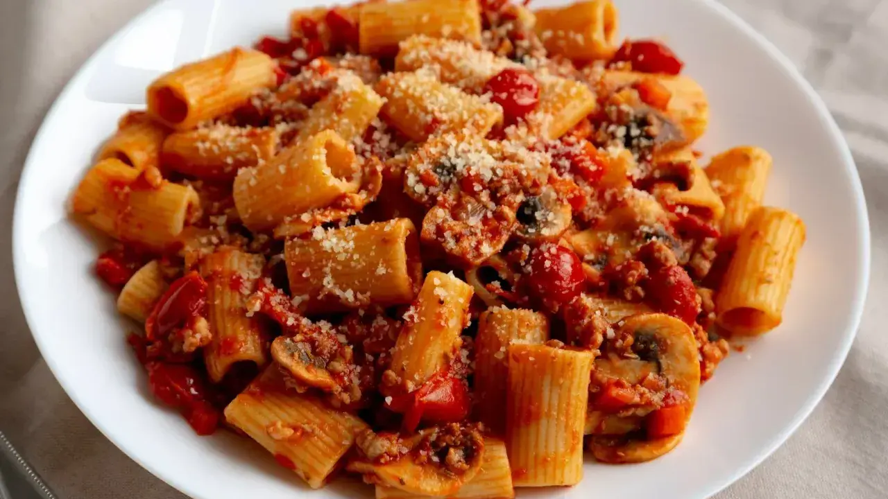Pyszny makaron z sosem pomidorowym, grzybami i parmezanem na białym talerzu.