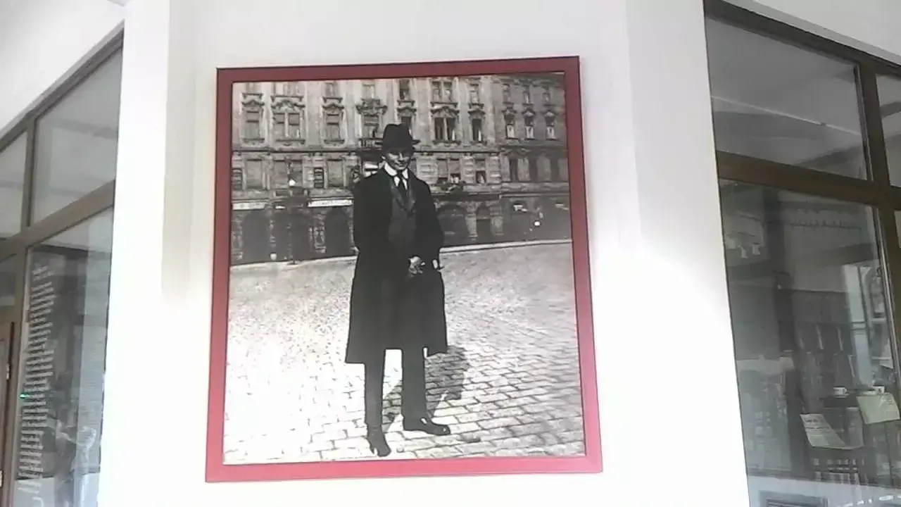 Ritratto di Franz Kafka, figura iconica che ci fa chiedere chi era Kafka, in piedi su un selciato con un edificio sullo sfondo.