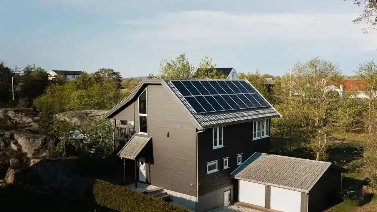 Ett modernt hus med mörk fasad och ett tak täckt av solceller. Bredvid huset finns ett garage med vita portar.