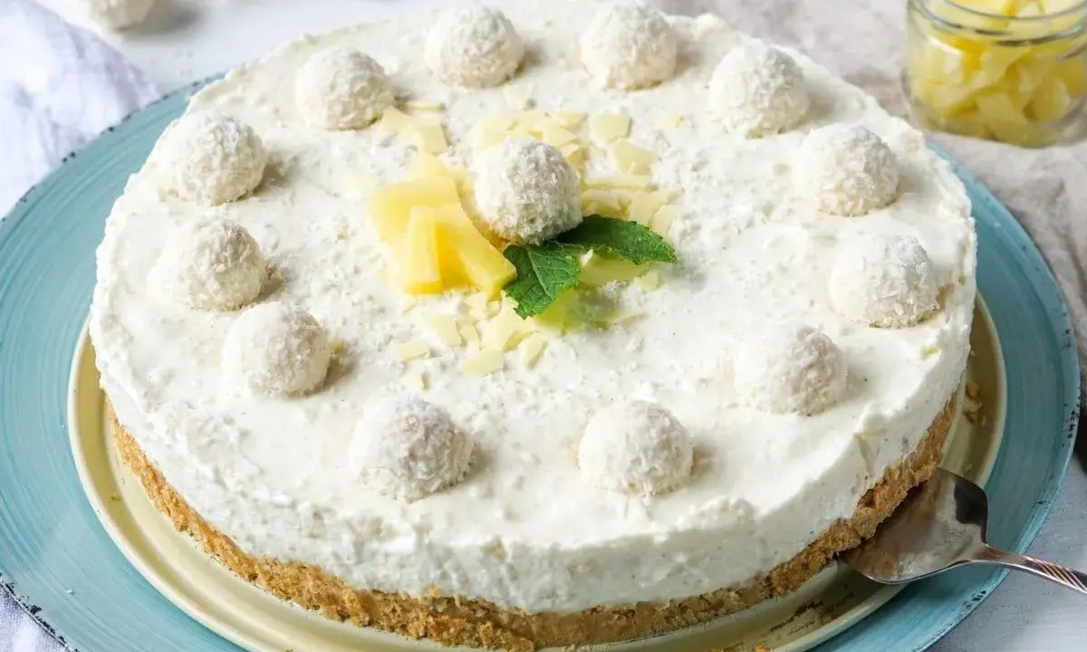 Eine köstliche Raffaello Torte ohne Backen, dekoriert mit Kokosbällchen, Ananas und Minze.