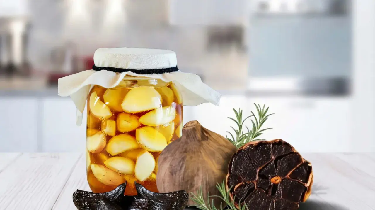 Ein Glas mit fermentiertem Knoblauch in Honig, daneben schwarzer Knoblauch und Rosmarin.