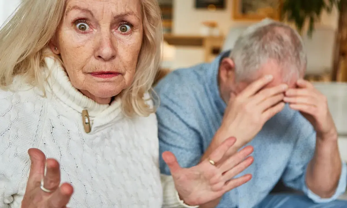Zmartwiona seniorka gestykuluje, podczas gdy jej partner ukrywa twarz w dłoniach. Może to symbolizować senność i brak apetytu u seniora.