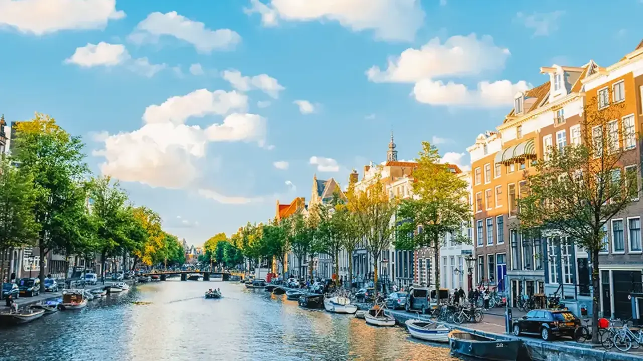 Widok na kanał w Amsterdamie, z łodziami, kamienicami i zielenią. Idealne miejsce, by poczuć, gdzie jest Amsterdam.