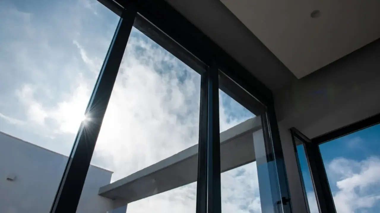 El sol brilla a través del vidrio guardian, iluminando un cielo azul con nubes blancas.