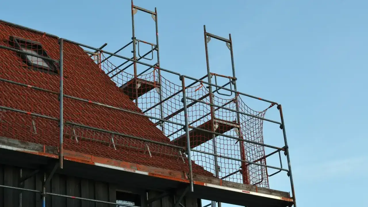 Metalowe rusztowanie na dachu z czerwonej dachówki, gotowe do prac remontowych.