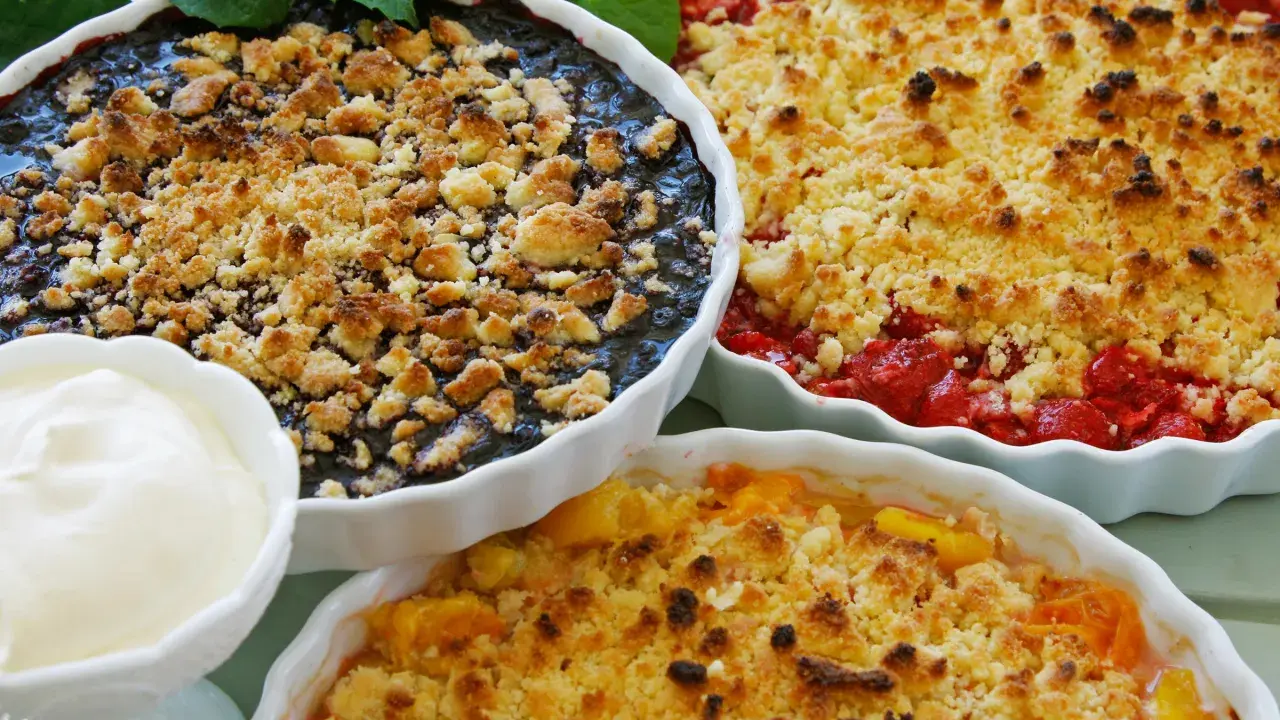 Tre ugnsbakade smulpajer med blåbär, jordgubbar och persika. Perfekt för ett smuldeg recept. Serveras med en klick grädde.