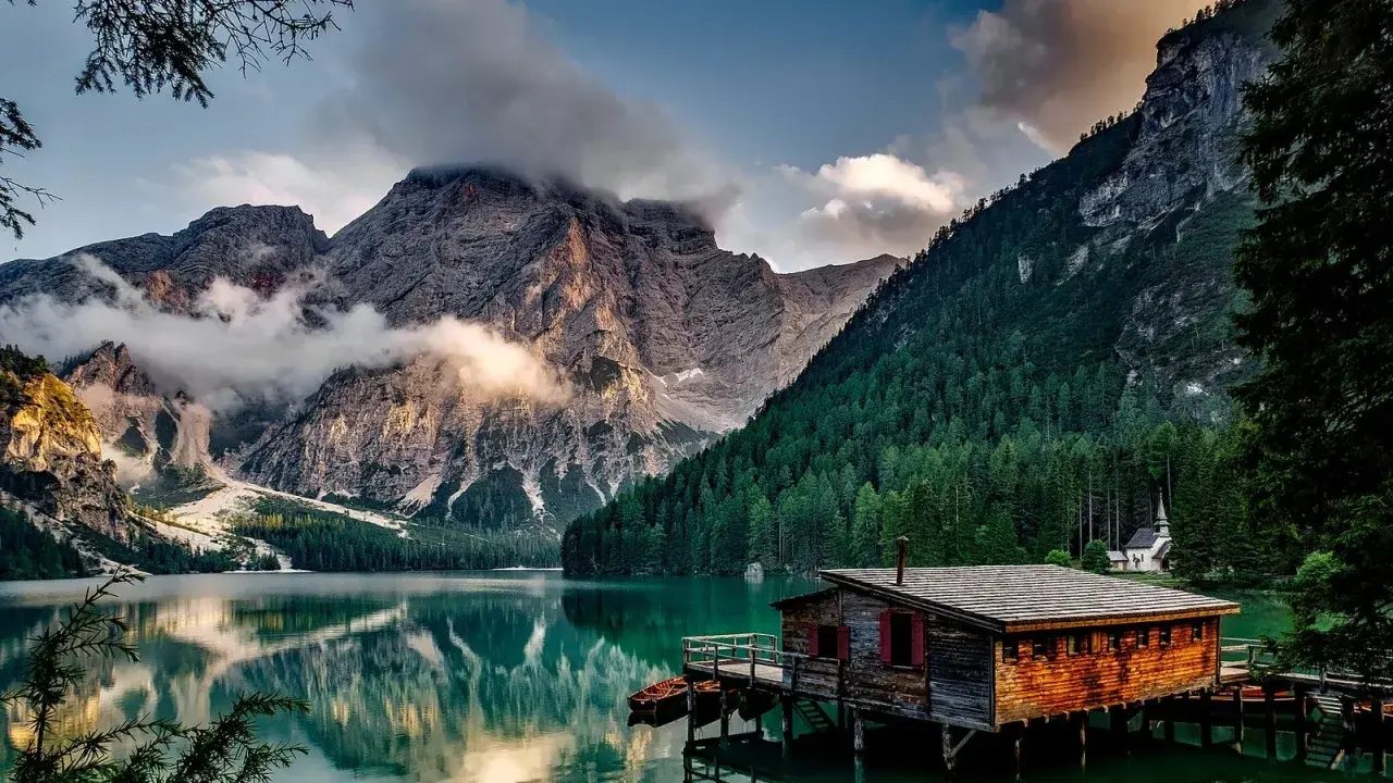 Lago alpino con baita in legno e montagne nebbiose. Curiosità sul Trentino Alto Adige: un luogo da fiaba.