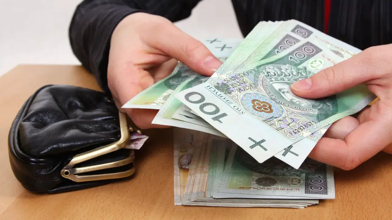 Dłonie liczą banknoty 100 zł obok portmonetki. Zastanawiasz się, ile wynosi trzynasta emerytura netto?
