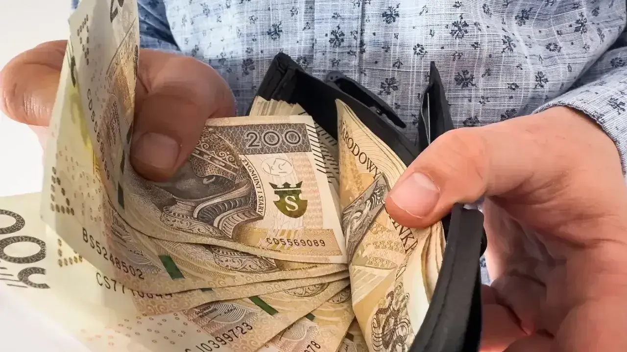 Ręce wkładają banknoty 200 zł do portfela. To może być nagroda jubileuszowa za długoletnią pracę.