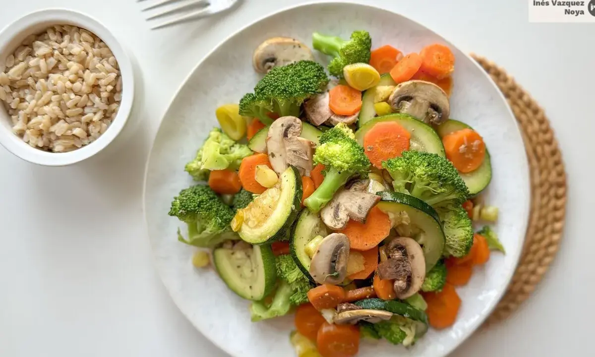 Un colorido salteado de verduras con brócoli, zanahoria, calabacín y champiñones, servido junto a un tazón de arroz integral.
