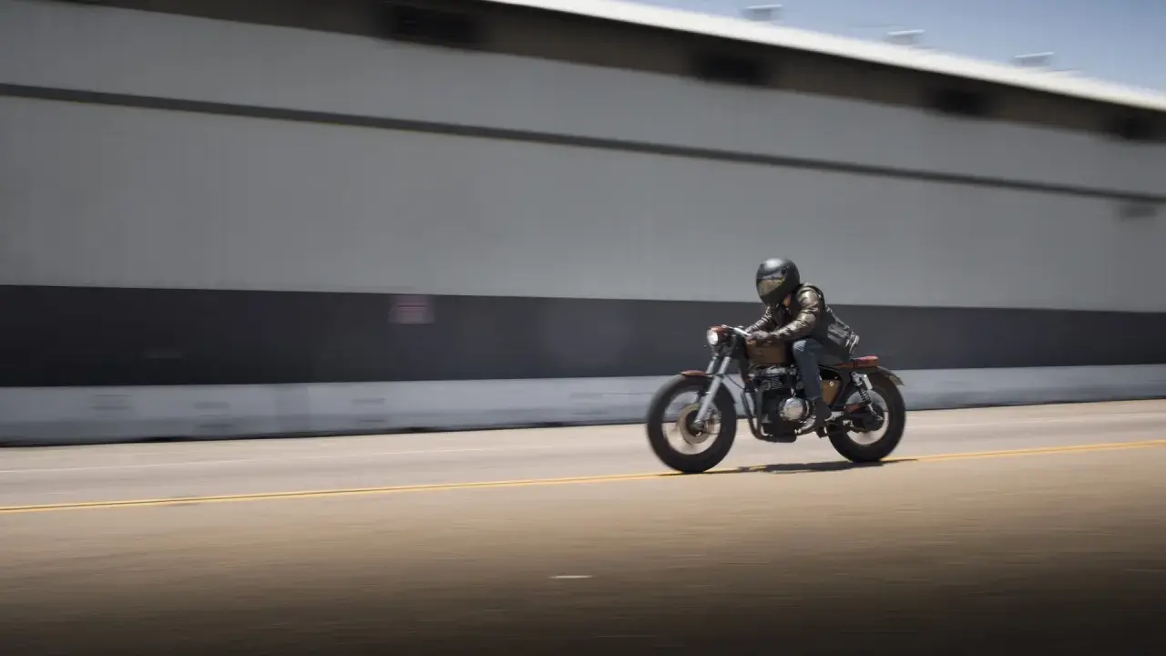 Motociclista con casco y chaqueta de cuero sobre una moto estilo cafe racer, en movimiento rápido por una carretera. El carmet a2 es su compañero de aventuras.