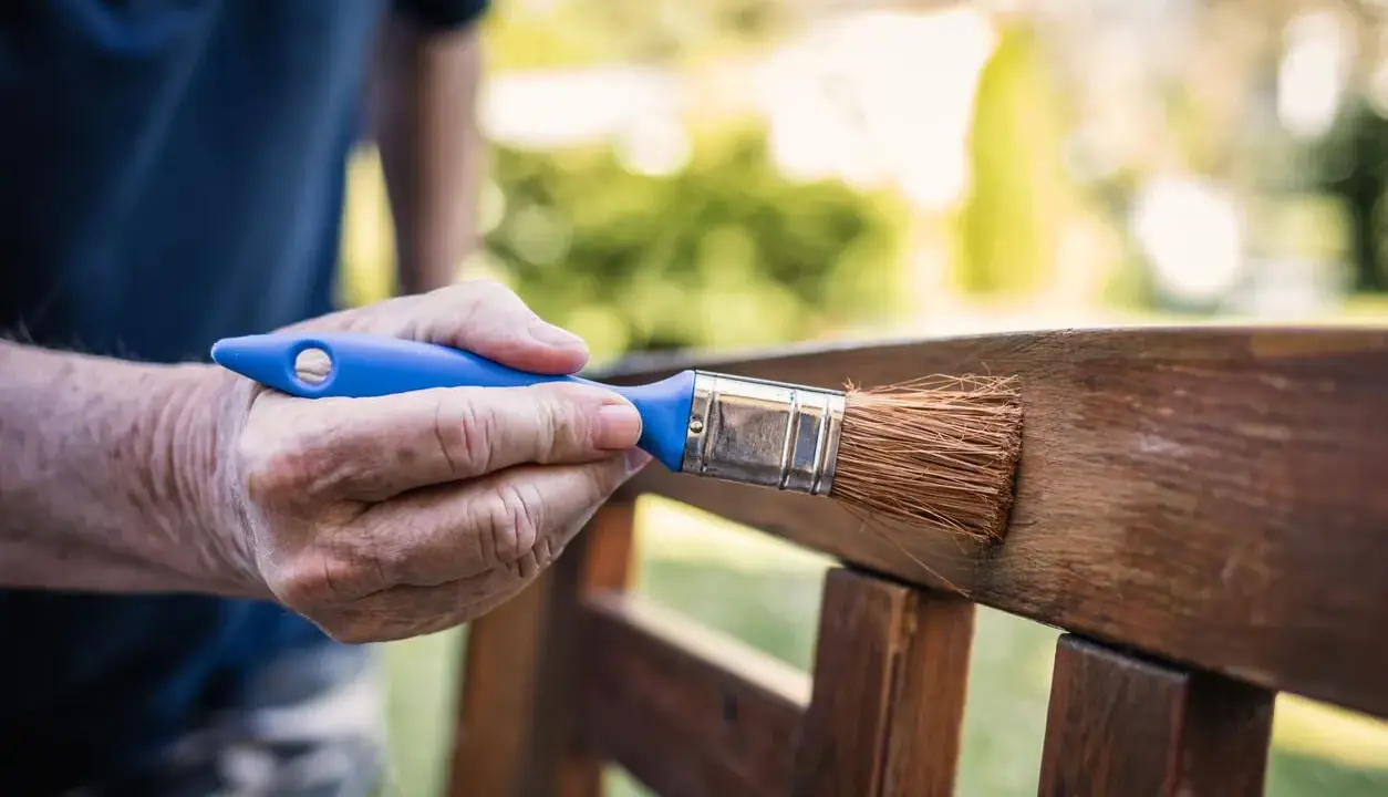 Mano aplicando barniz a un banco de jardín, creando un hermoso efecto madera.