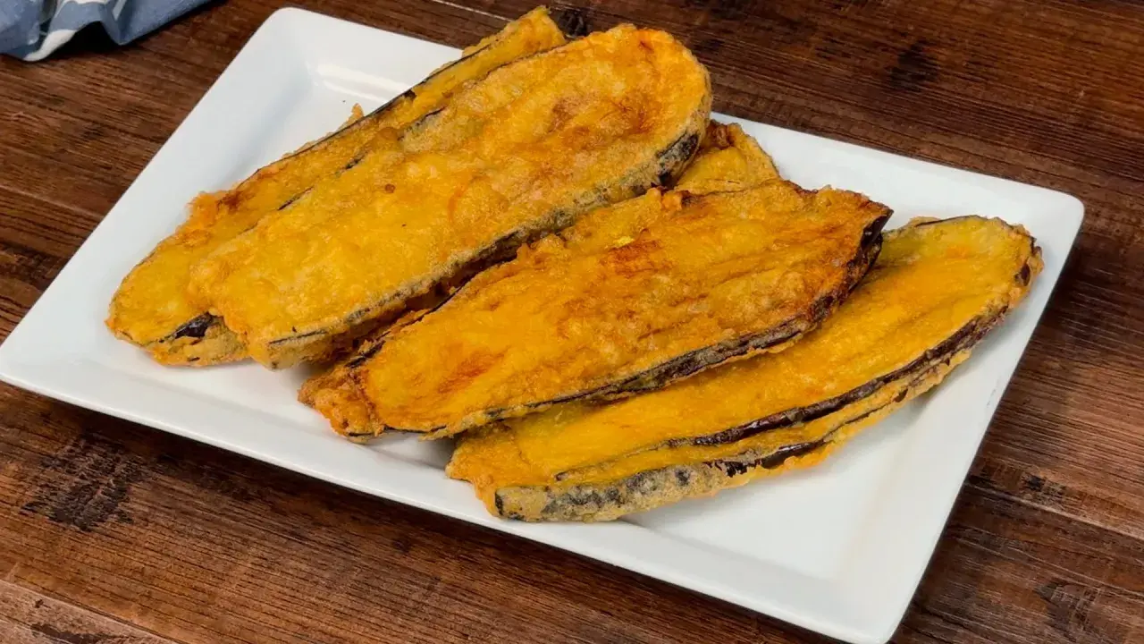 Fette di melanzane fritte, dorate e croccanti, servite su un piatto bianco. Un assaggio delle deliziose melanzane alla pullastiello.