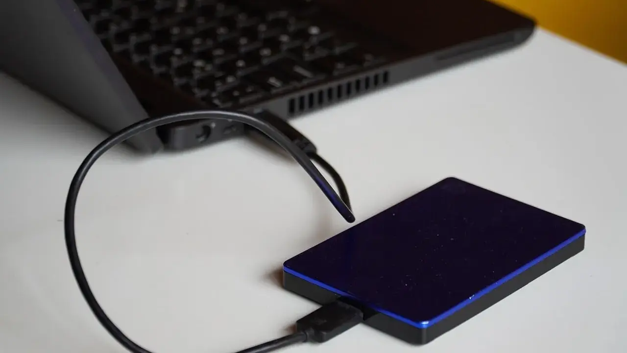 Un disque dur externe bleu est connecté à un ordinateur portable. Un guide pour comment choisir un disque dur.
