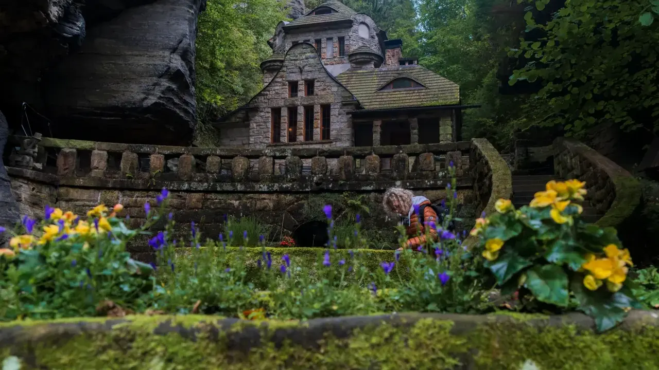 Kamienny domek w sercu Szwajcarii Czeskiej, otoczony bujną zielenią i kwitnącymi kwiatami.